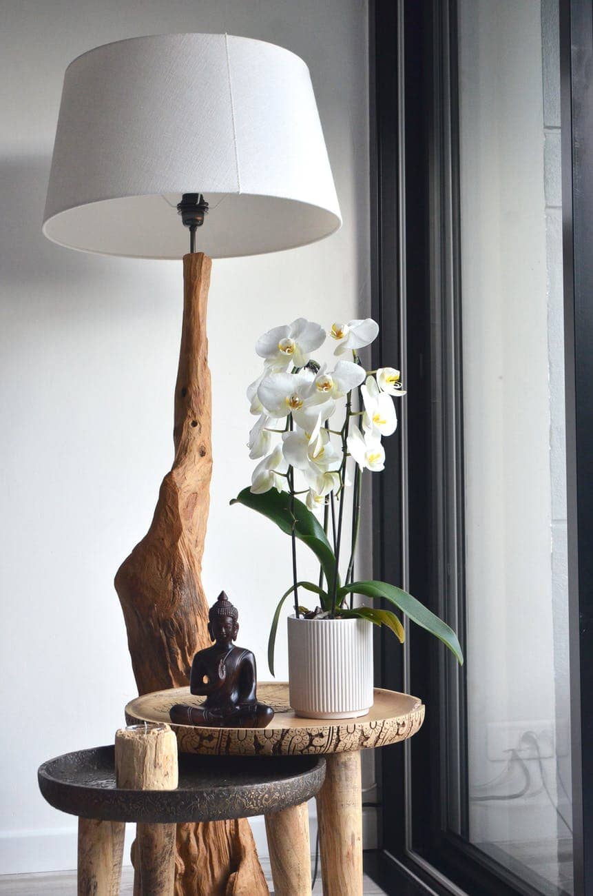 big wooden lamp placed near table with potted orchids and buddha statuette